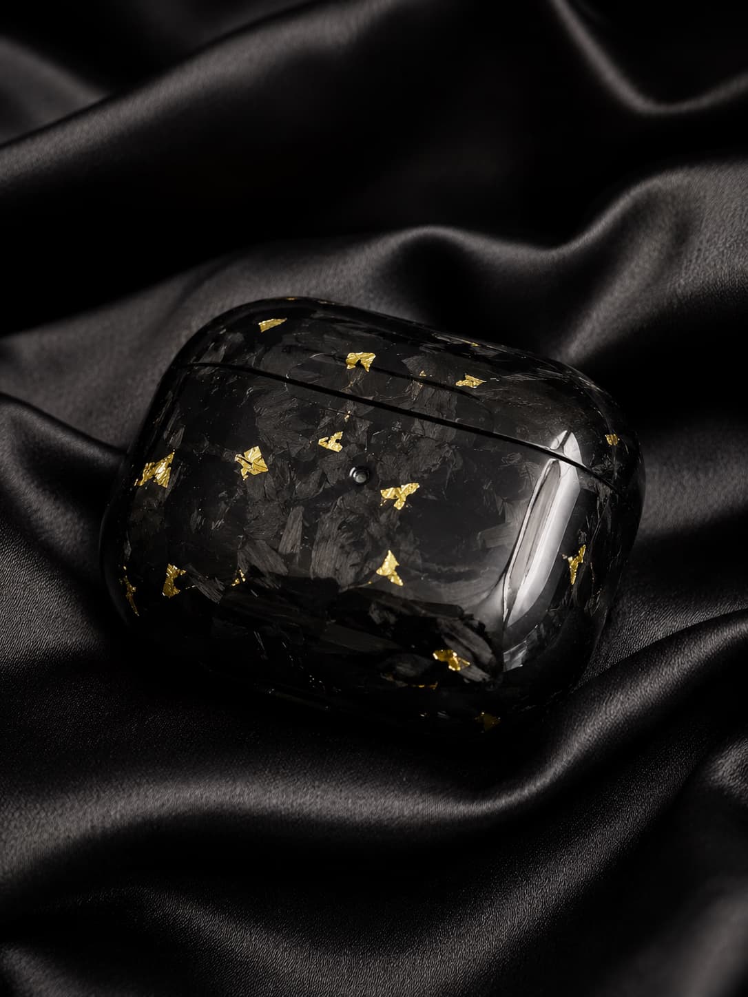 Obsidian-Gold-AirPods-Case mit glänzender Carbonstruktur auf schwarzem Satin